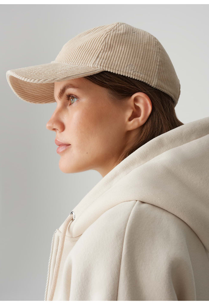 Woman wearing a beige cap and coat against a plain background