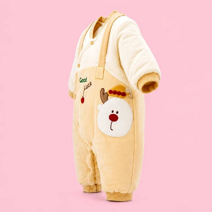 A baby one-piece fleece sleeper in Mustard and cream , featuring an applique reindeer face on the leg and 'Good Luck' text with a cherry on the chest, set against a solid pink background.