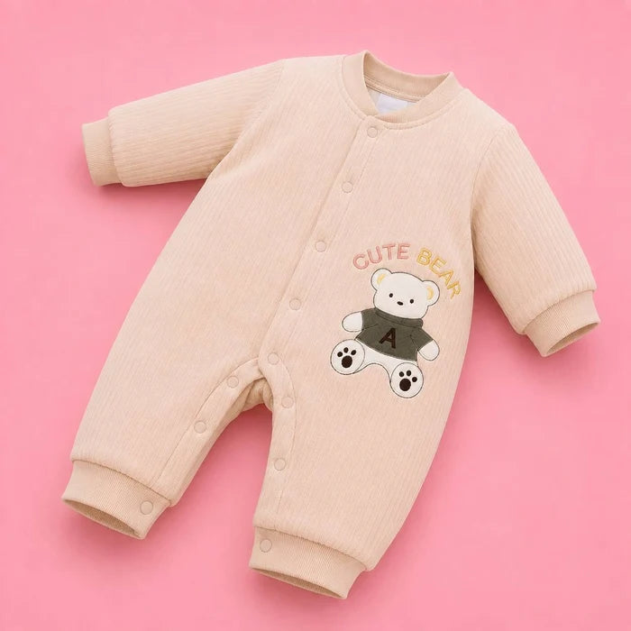 A baby long-sleeve ribbed romper in a light peach-beige color, featuring a cartoon bear graphic with the text 'CUTE BEAR' on the chest, laid flat on a solid pink background.