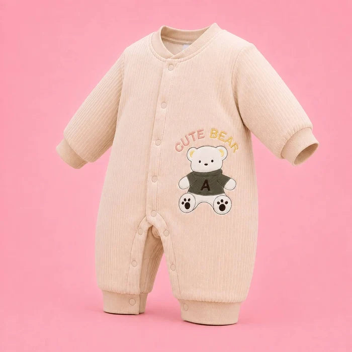 A baby long-sleeve ribbed romper in a light cream-beige color, featuring a cute embroidered white bear wearing a dark green sweater with the letter 'A' on the chest, and 'CUTE BEAR' embroidered above it. The romper is displayed on a solid pink background.