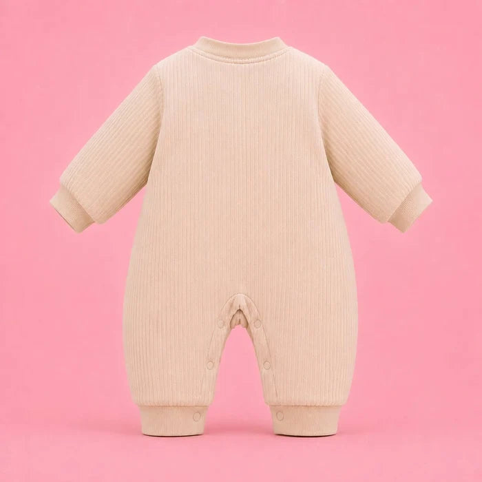 A cream-colored ribbed knit baby jumpsuit with long sleeves and an open crotch, shown from the back against a solid pink background.