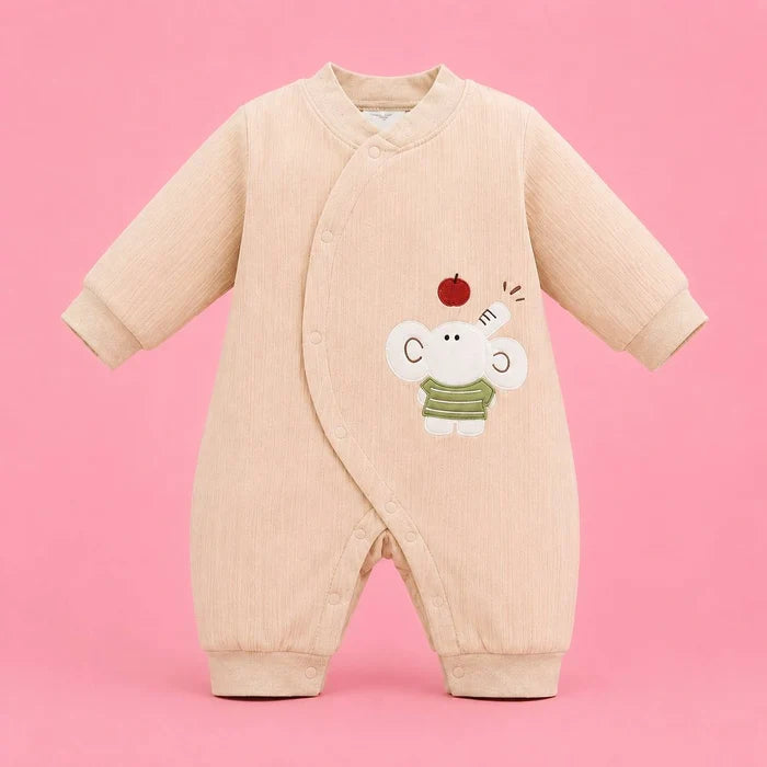 A long-sleeve baby romper in a light beige corduroy fabric, featuring a cute embroidered elephant character wearing a green striped shirt with a small red apple on its head, set against a solid pink background.