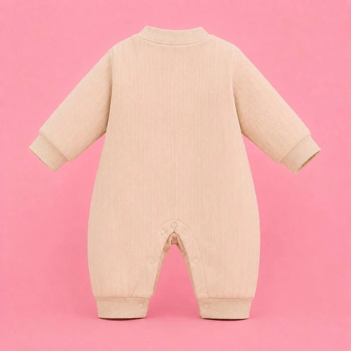 A light beige ribbed corduroy baby jumpsuit shown from the back, featuring long sleeves, ribbed cuffs, and snap closures at the crotch, set against a solid pink background.