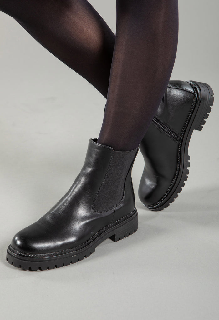 A person wearing black Chelsea boots with a visible 4cm block heel and elasticated panel.