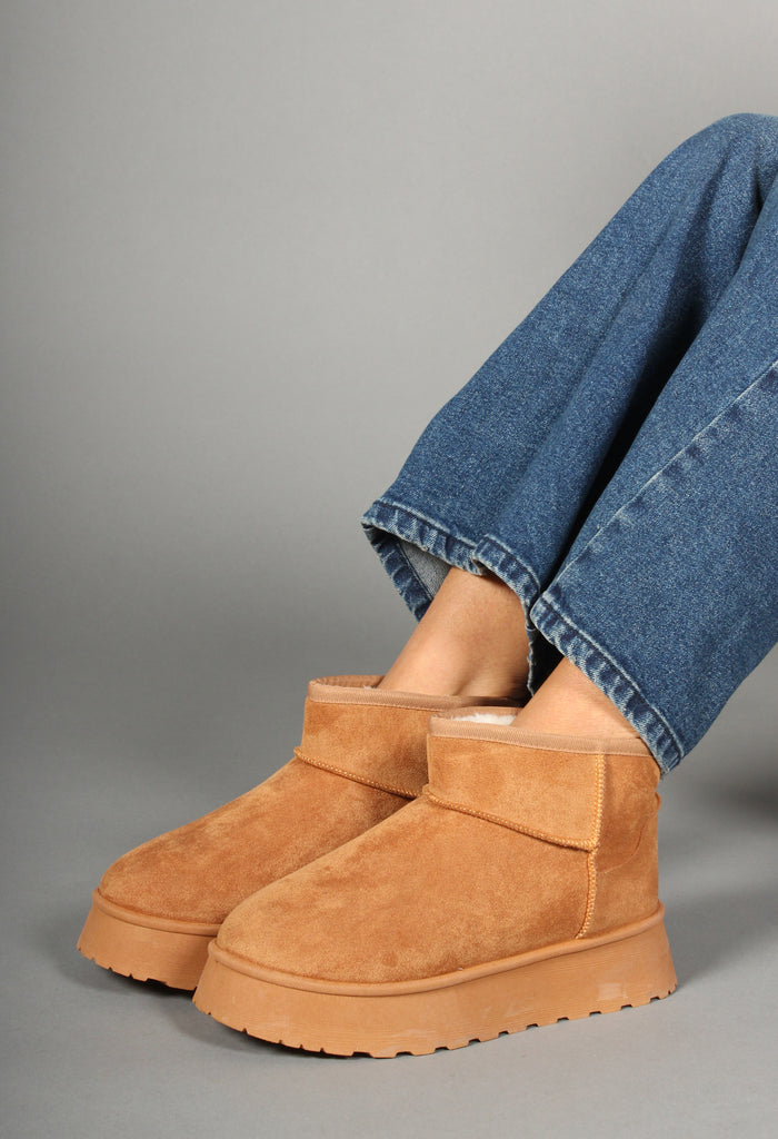 A woman is seated wearing camel faux fur lined platform boots with a round toe design.