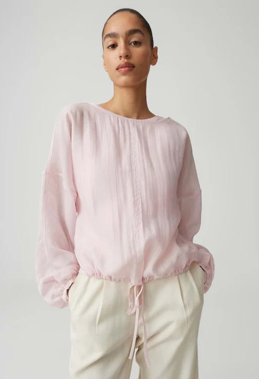 Person wearing a light pink blouse with long sleeves on a plain background