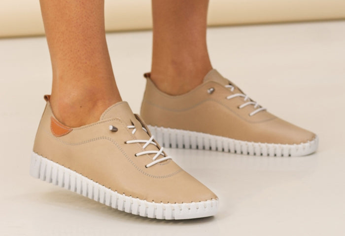 A pair of beige leather Plimsoll shoes with a lace-up closure, displayed on a person standing against a white background.