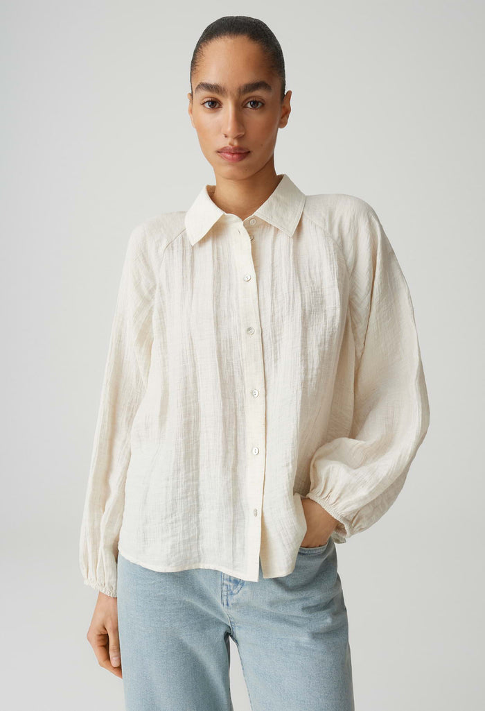 Woman wearing a white button-up shirt and light blue jeans against a plain background