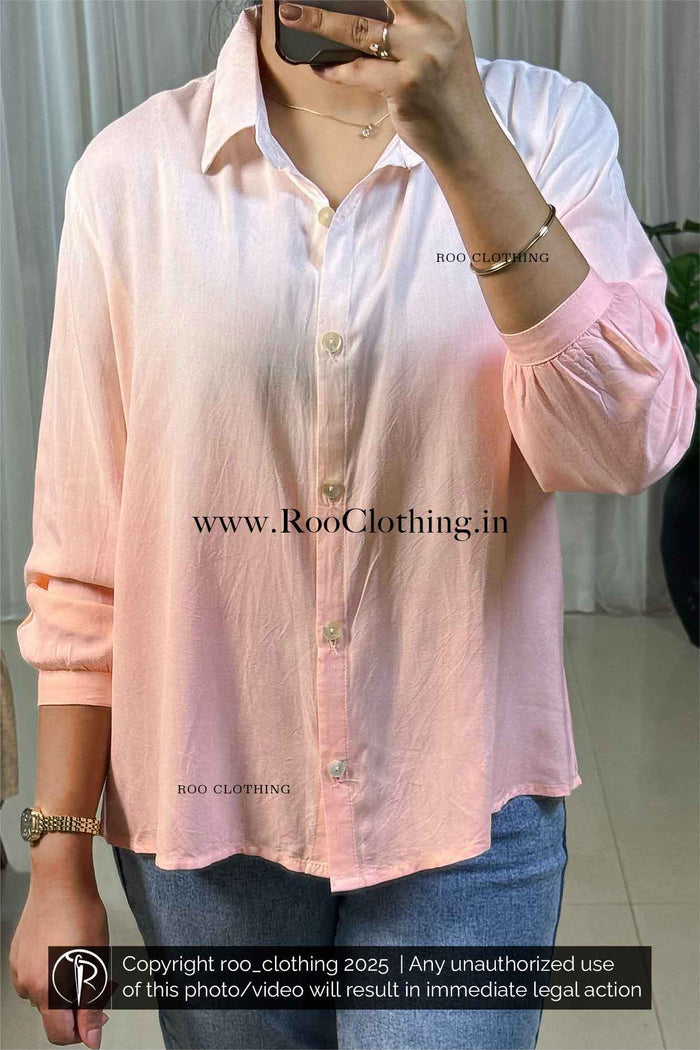 Person wearing a light pink shirt with rolled-up sleeves, taking a mirror selfie.