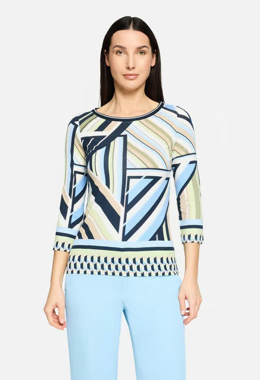 Woman wearing a patterned top and light blue pants on a white background