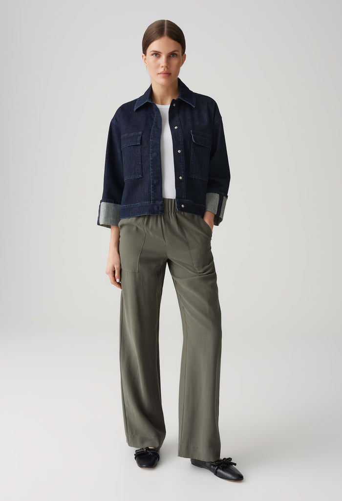 Person wearing a navy denim jacket, white shirt, and olive green pants on a light gray background
