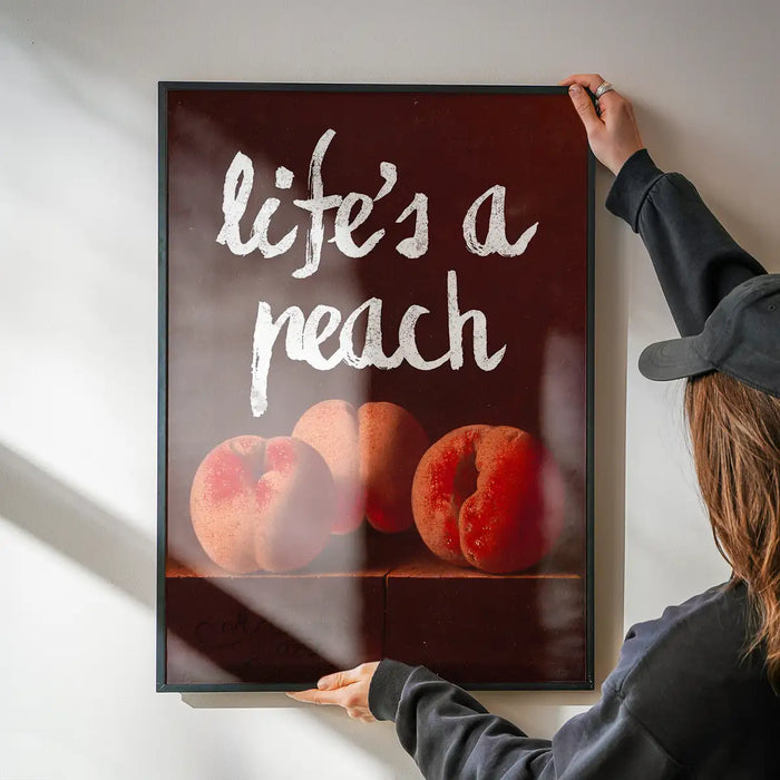 Life's A Peach Altered Art Print being hung on a wall in a black frame