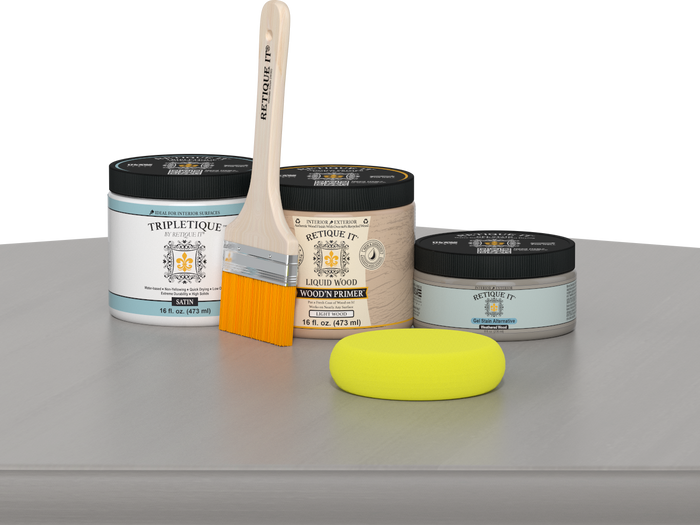 Retique It® Weathered Wood Multipurpose Kit contents with Liquid Wood primer, Weathered Wood gel stain alternative, Tripletique satin interior top coat, paintbrush, and yellow sponge displayed on a gray wood surface.