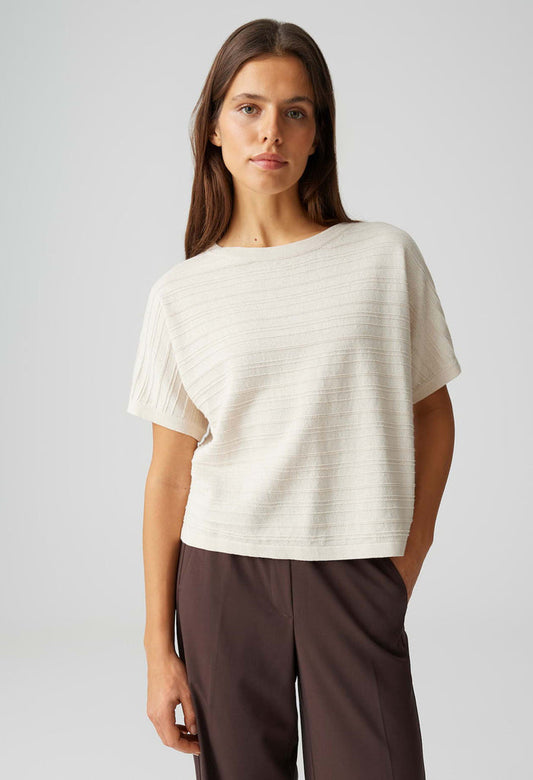 Woman wearing a white top and brown pants on a light gray background