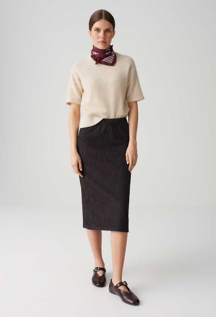 Woman wearing a beige sweater and black skirt with a red scarf on a white background