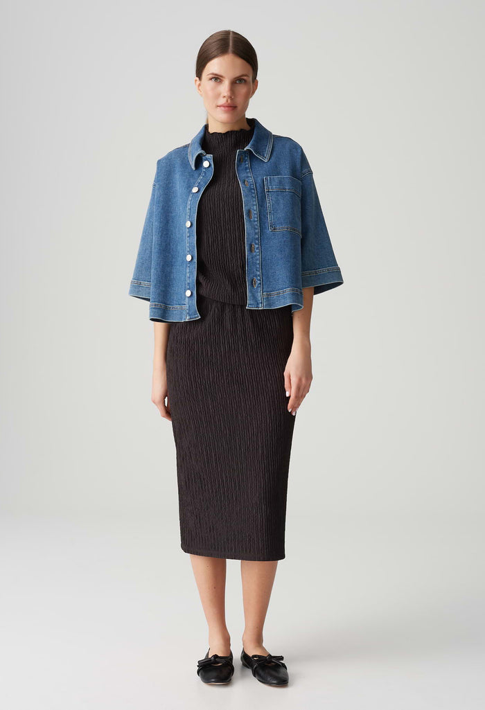 Woman wearing a blue denim jacket over a black outfit on a white background