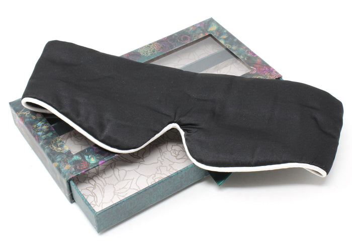 Black sleep mask with white trim on a decorative box