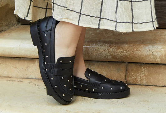 Black loafers with silver studs worn by a person on stone steps.