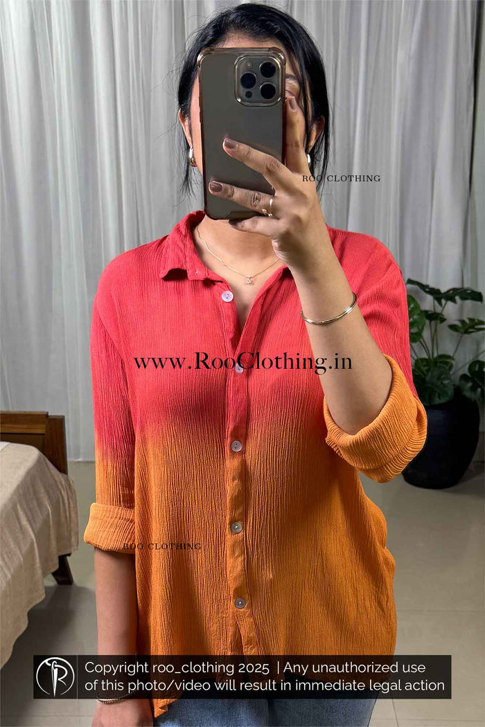 Person wearing a red and orange shirt taking a mirror selfie with a blurred background.