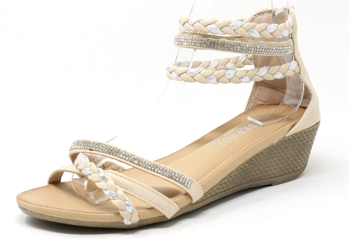 A beige-colored wedge sandal with triple ankle straps and a rhinestone-embellished strap across the foot. The sandal features a open toe design and a comfort sole.